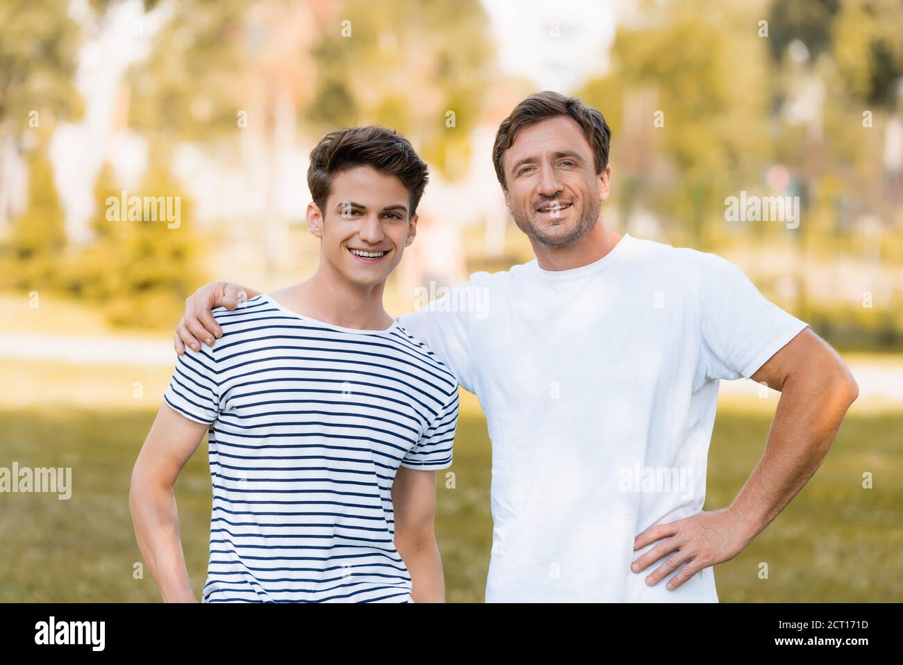man standing with hand on hip and hugging teenager son outside Stock Photo