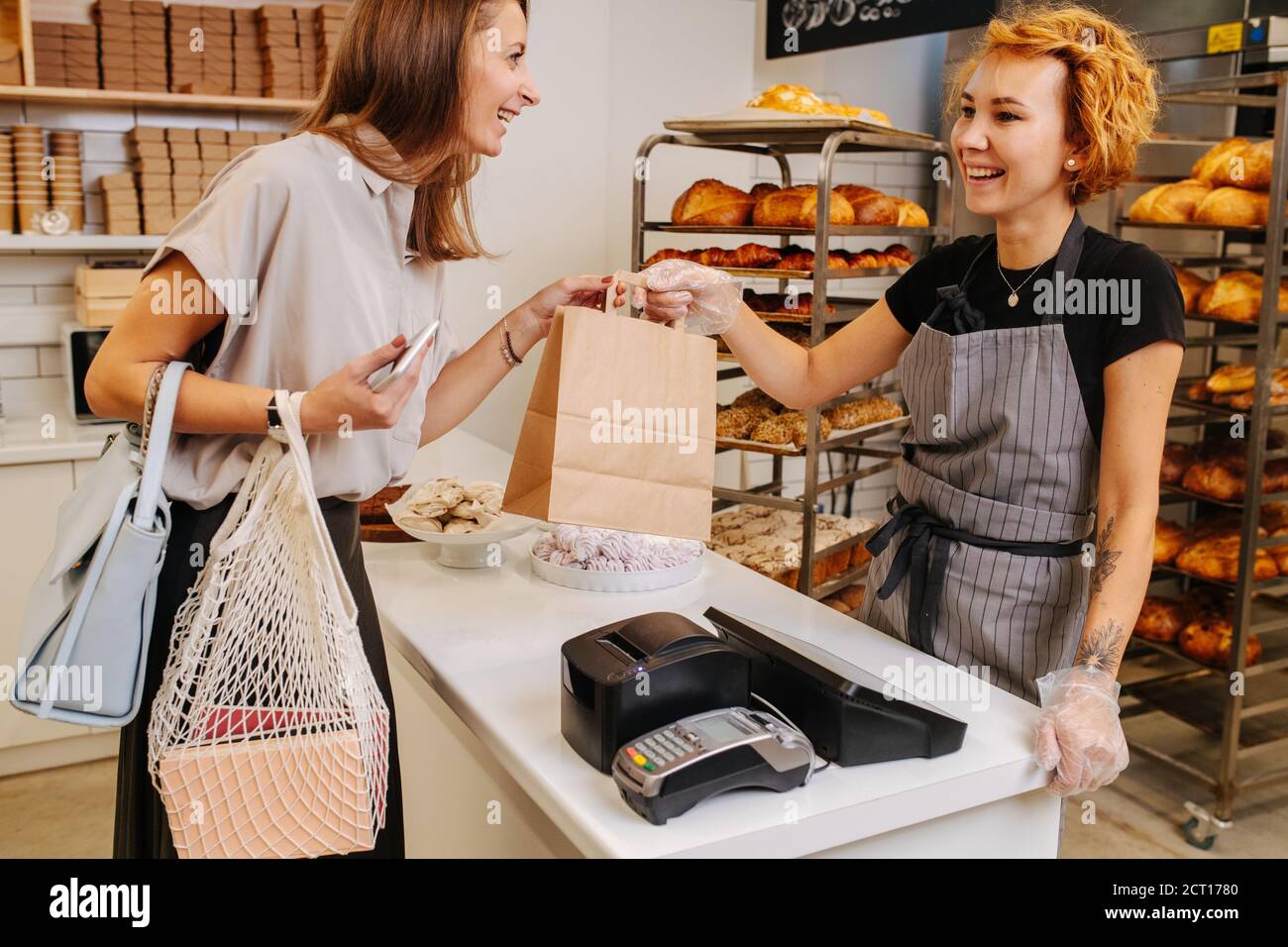 Female client in a bakery shop receiving paper bag with items she bought. Stock Photo