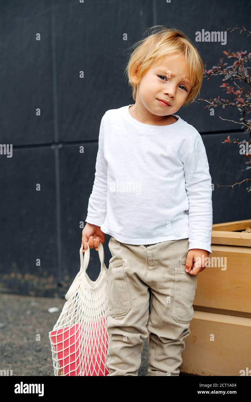 Little boy with blond hair holding net bag, outdoors on the street Stock Photo