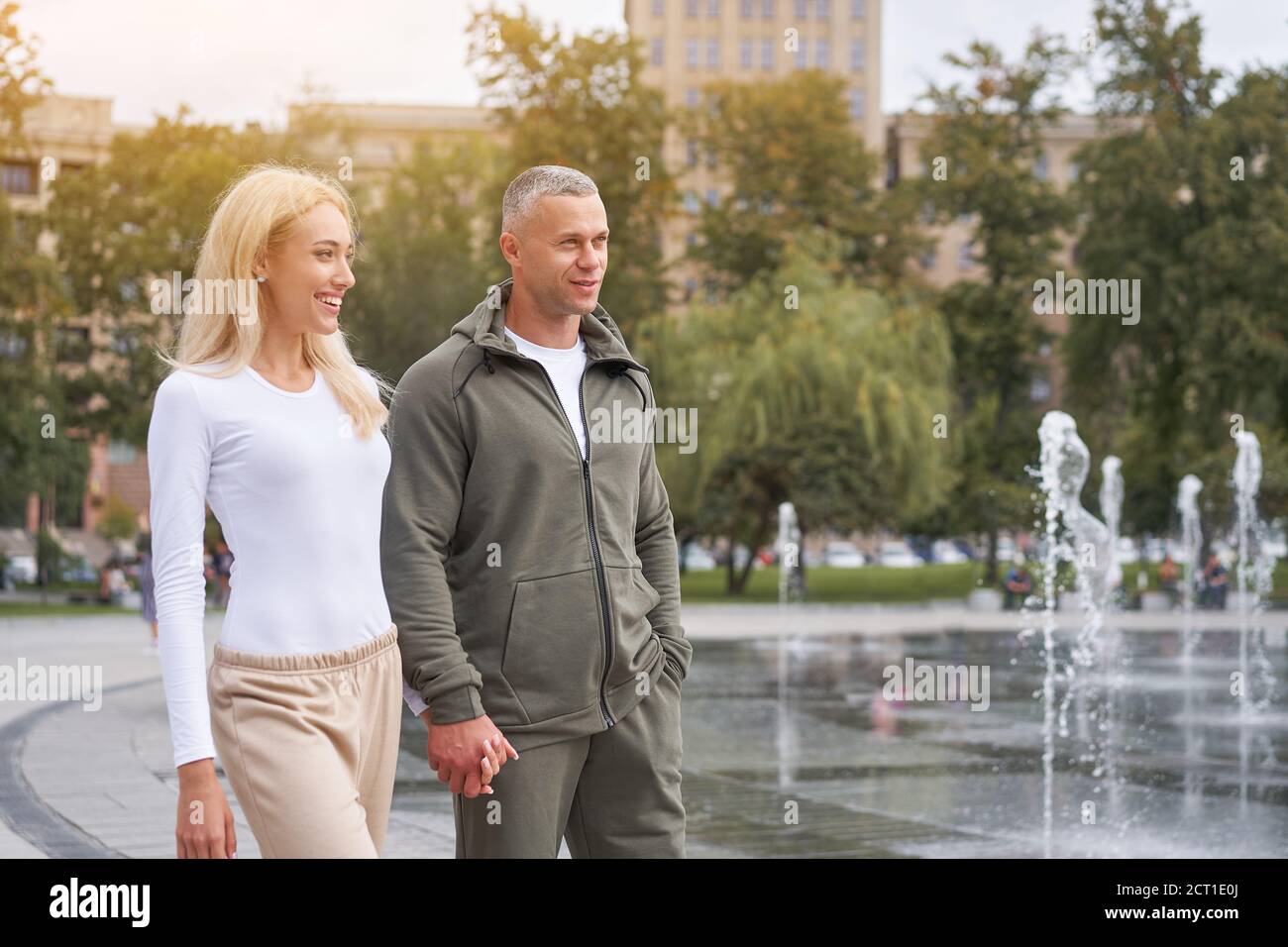 Couple in love walking outdoors park fountain Caucasian man woman walk outside after jogging dressed sport clothes  Healthy livestyle Hold hands each Stock Photo