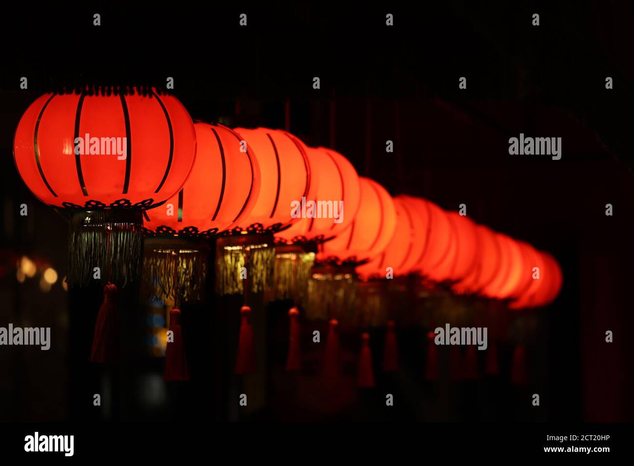 Red Chinese lanterns glow in a row on a night street, selective focus Stock Photo
