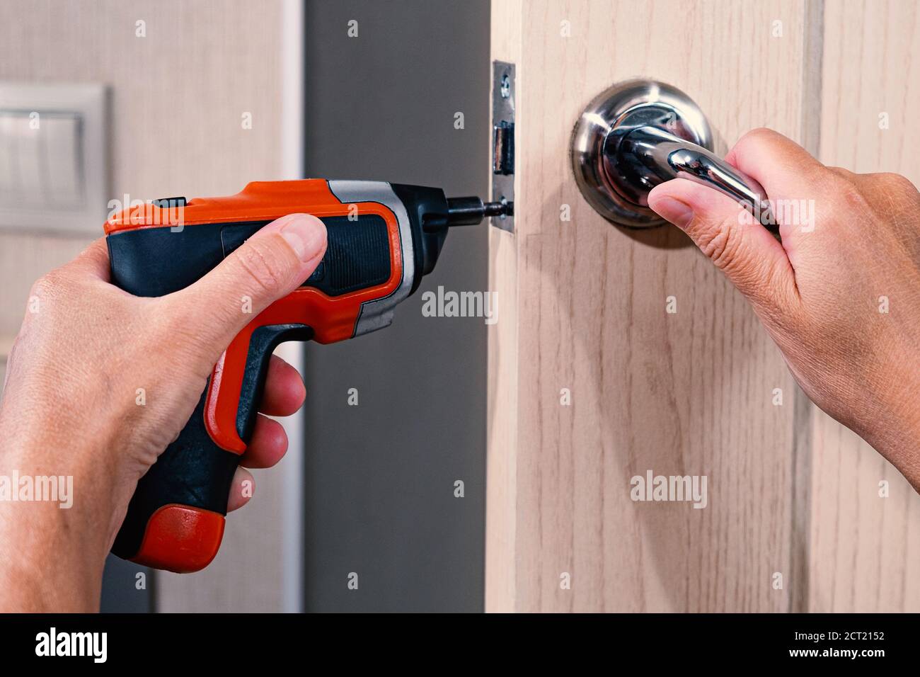 Repair of the door handle. The master clamps the loose screw with an electric screwdriver. Stock Photo