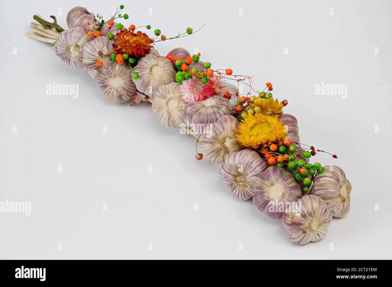 a braid of garlic, decorated with flowers, against a light background, photographed close up Stock Photo