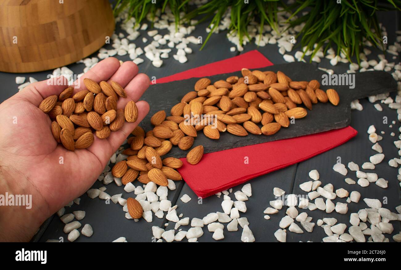 Almonds held by a white hand and taken from a sample table with more almonds, slate material, and decorated with white quartz stones Stock Photo
