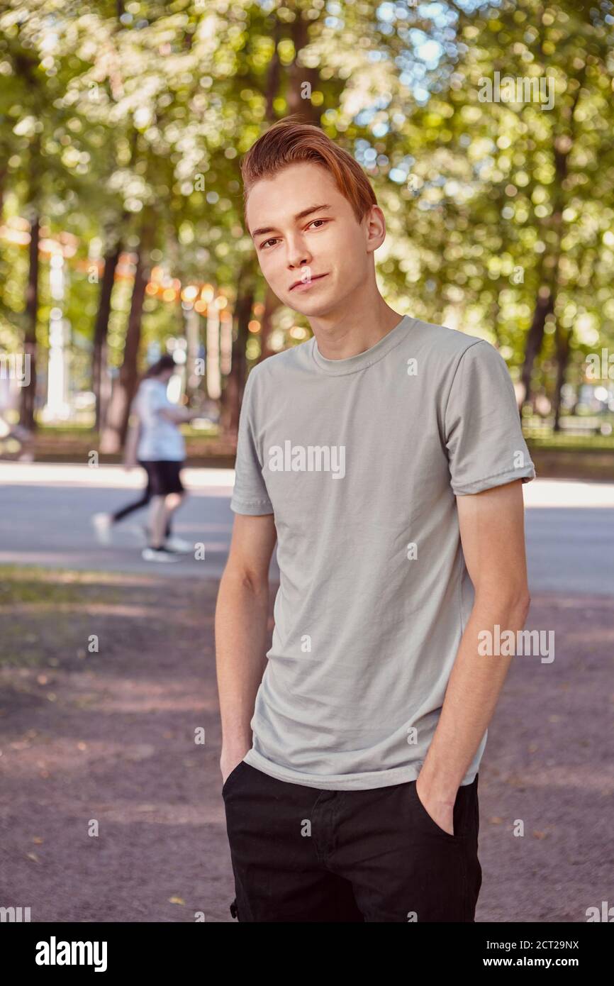 Young caucasian handsome man is standing in the public park on the blurred background. Stock Photo