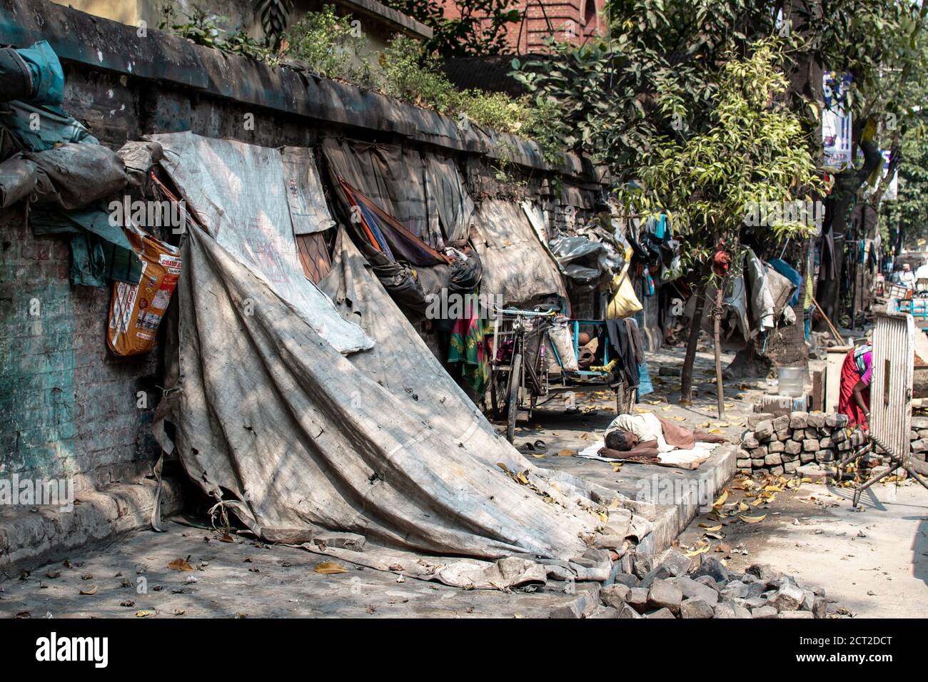 Kolkata, India - February 1, 2020: An unidentified man sleeps on the ground next to run down tarp shelter homes on February 1, 2020 in Kolkata, India Stock Photo