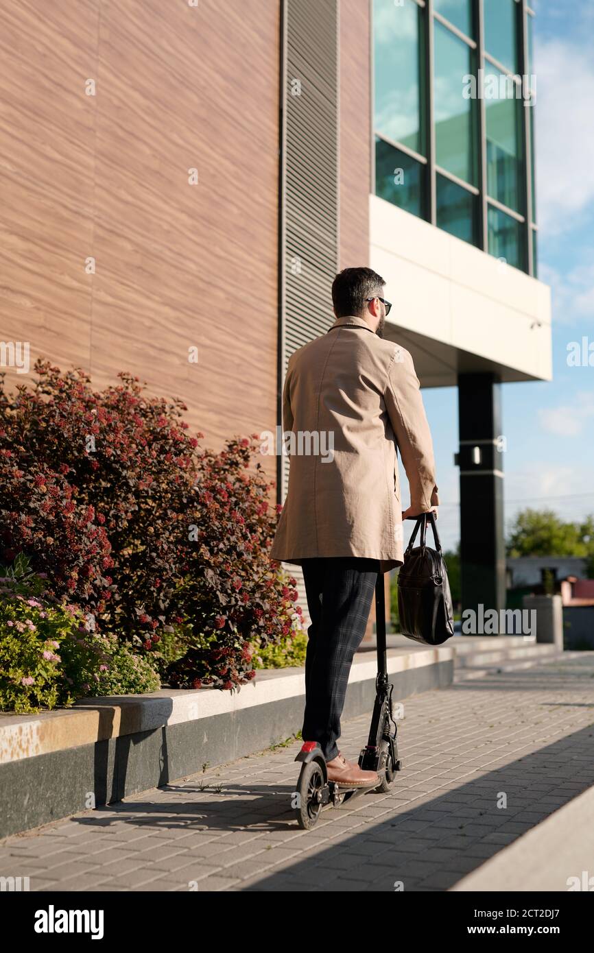 Rear view of contemporary businessman in smart casualwear riding on scooter Stock Photo