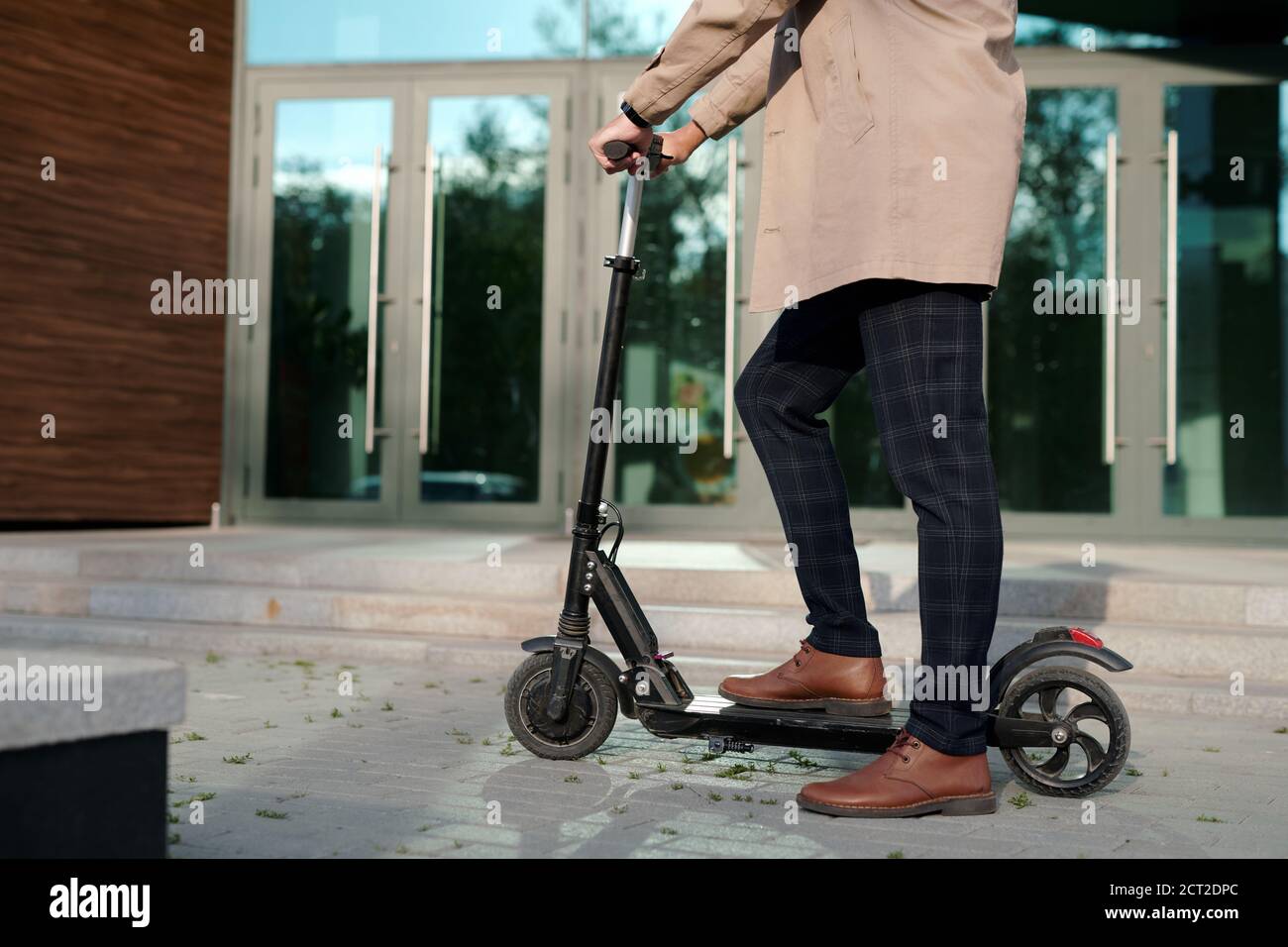 Low section of businessman in trenchcoat and pants holding by handles of scooter Stock Photo