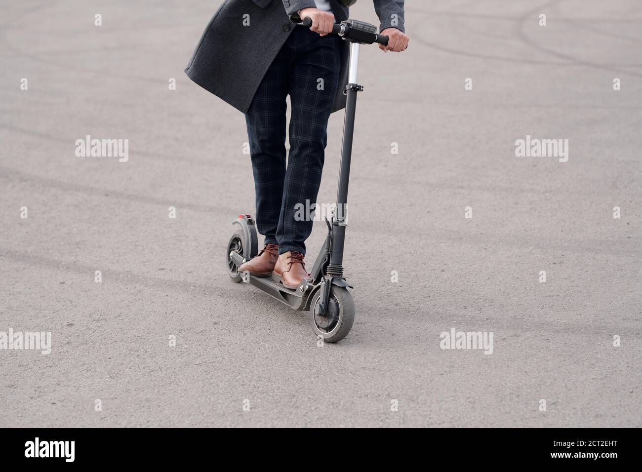 Low section of modern businessman in coat and pants riding electric scooter Stock Photo