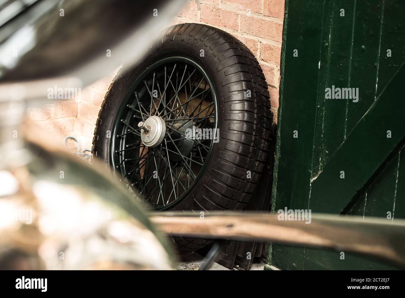 A Bentley 4 1/2 Litre Supercharged (The Green Hornet) Wire wheel leaning up against a brick wall in a garage at the Bicester Heritage Sunday Scramble. Stock Photo