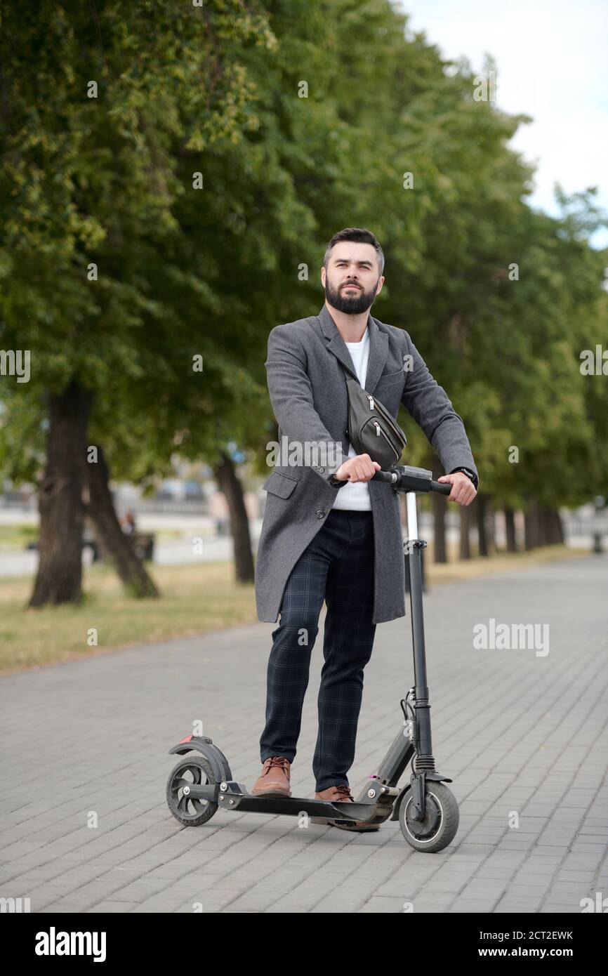 Young elegant businessman standing on electric scooter in urban environment Stock Photo