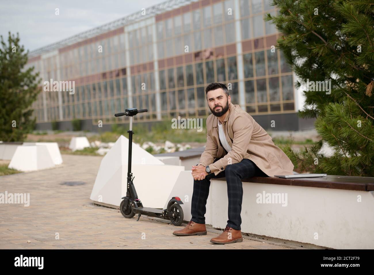 Young bearded businessman in smart casualwear having rest by coniferous tree Stock Photo