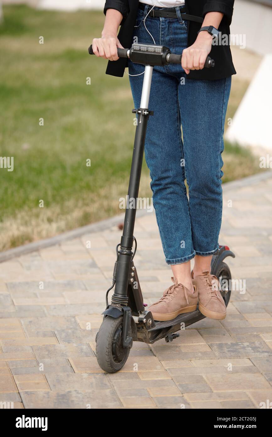 Contemporary young businesswoman in casualwear standing on electric scooter Stock Photo