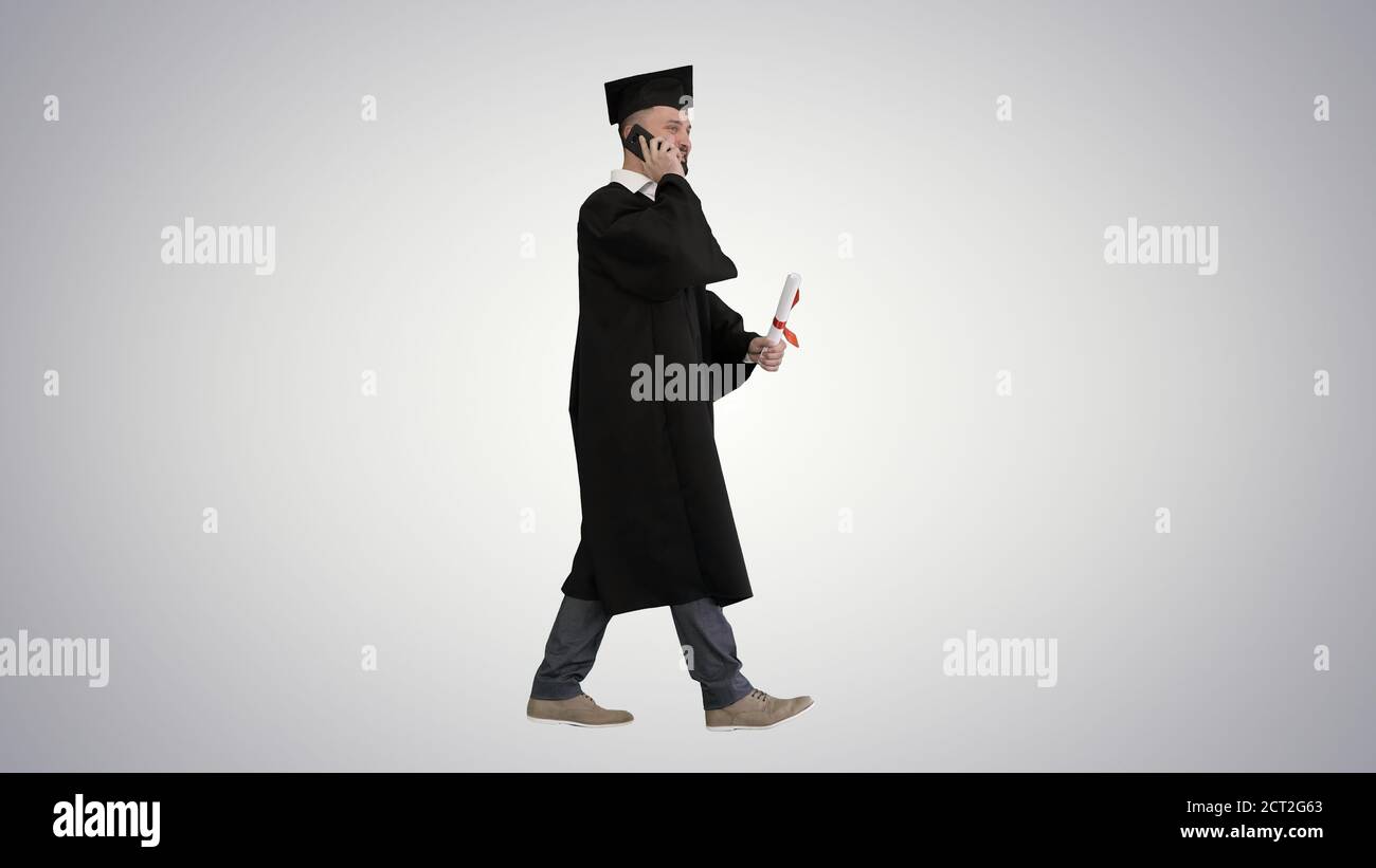 Graduating student walking and making a call on gradient backgro Stock Photo
