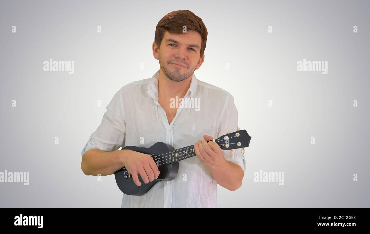Smiling young man playing ukulele looking into the camera on gra Stock Photo