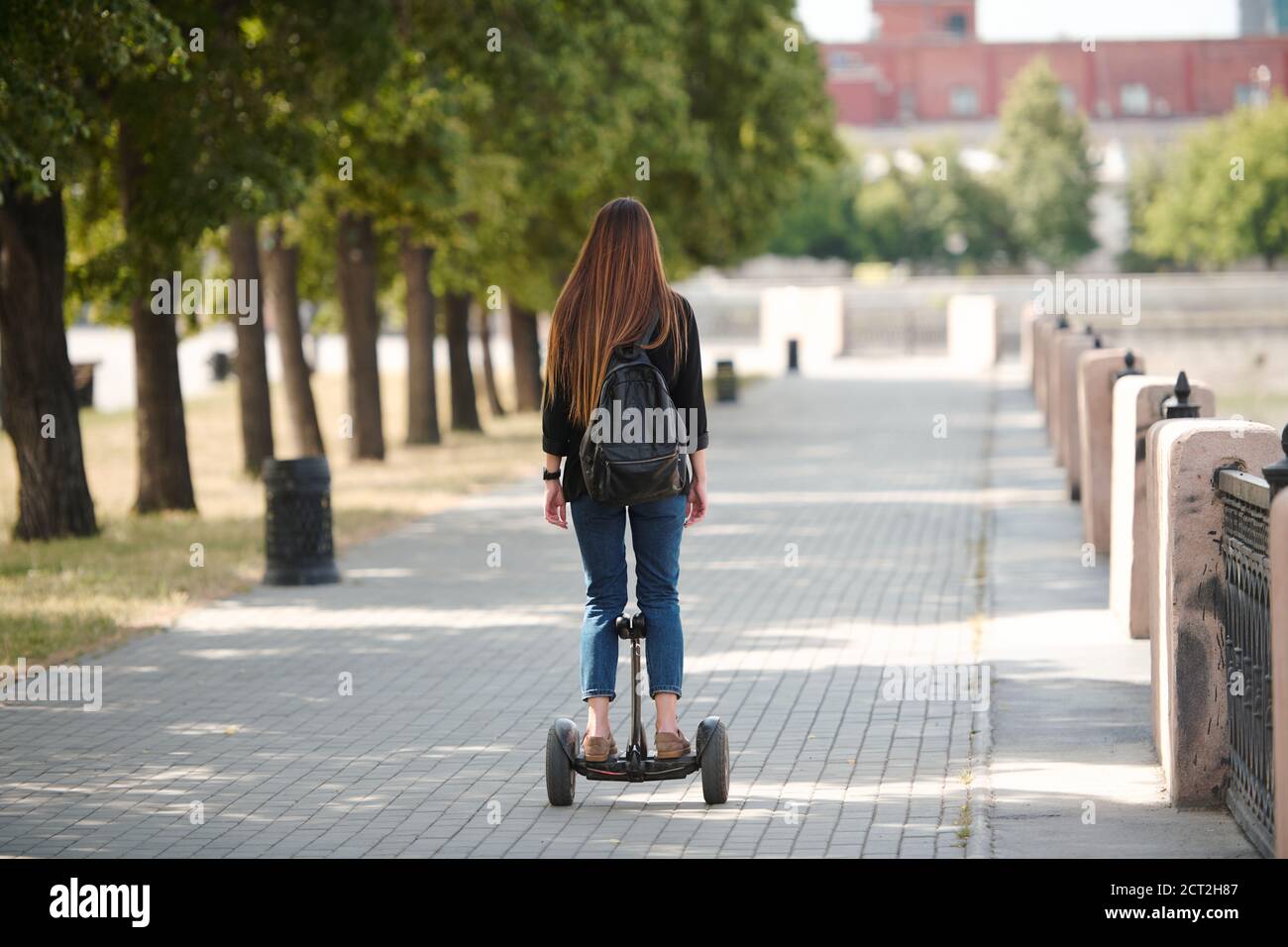 Back view of contemporary young businesswoman riding on gyroscope along road Stock Photo