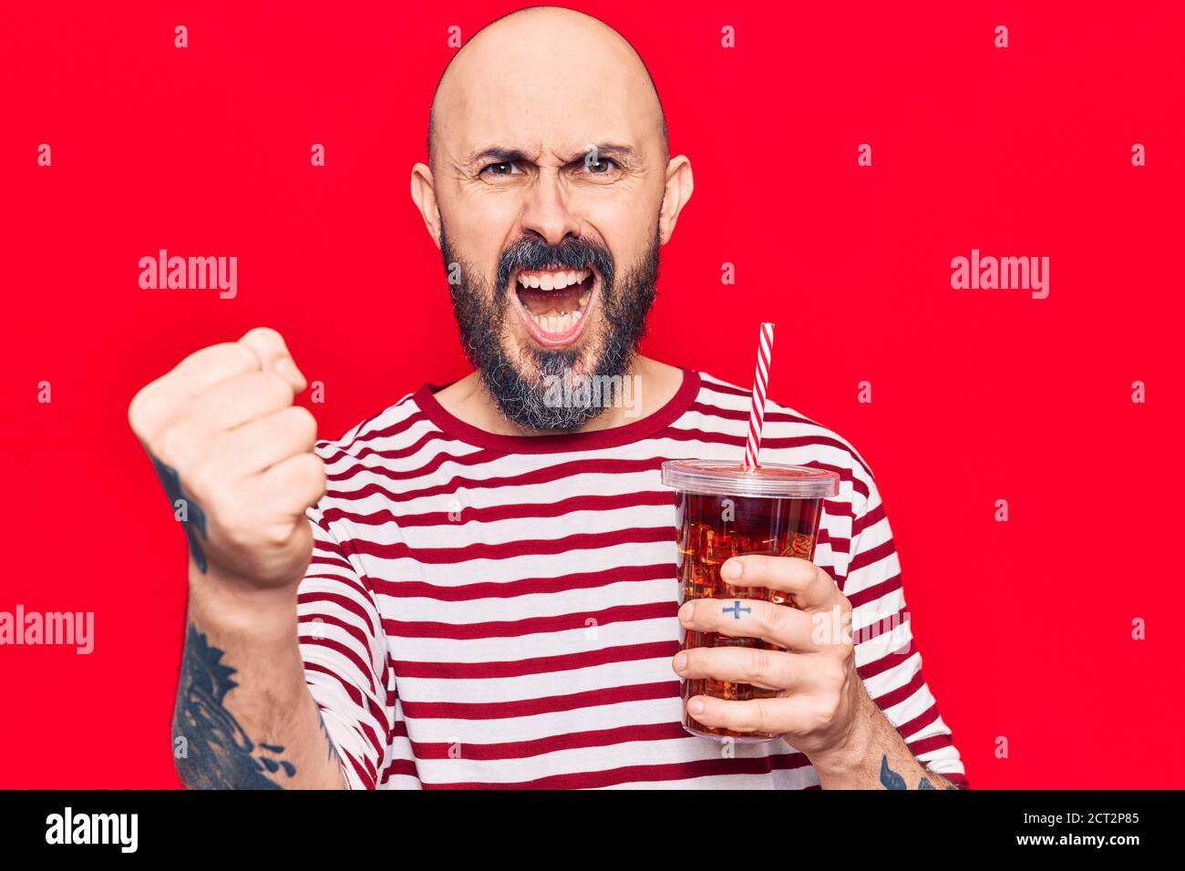 Young handsome man drinking glass of cola beverage annoyed and ...