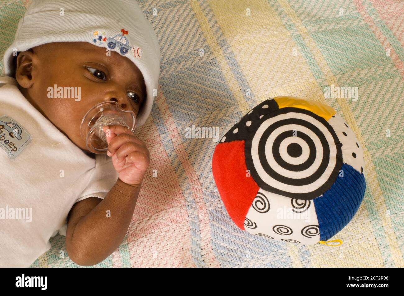 6 week old newborn baby boy one month premature alert looking at toy with high contrast black and white pattern, wearing cap and sucking on pacifier Stock Photo
