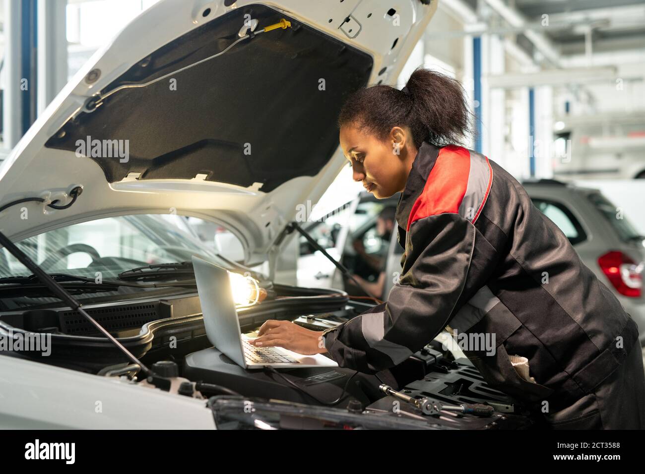 Young worker of car maintenance service bending over open engine compartment Stock Photo
