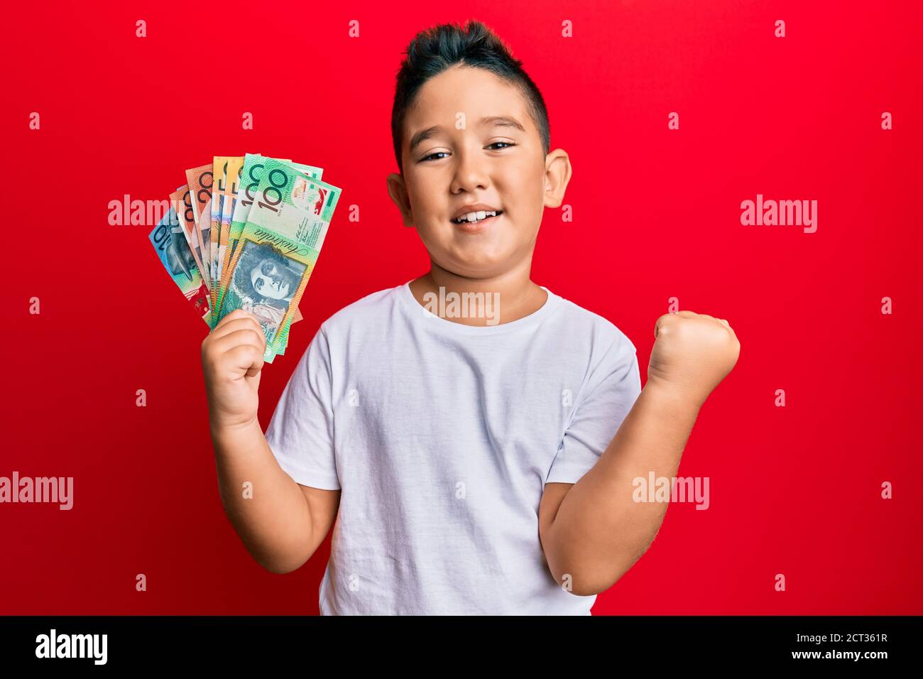Little boy hispanic kid holding australian dollars screaming proud, celebrating victory and success very excited with raised arm Stock Photo