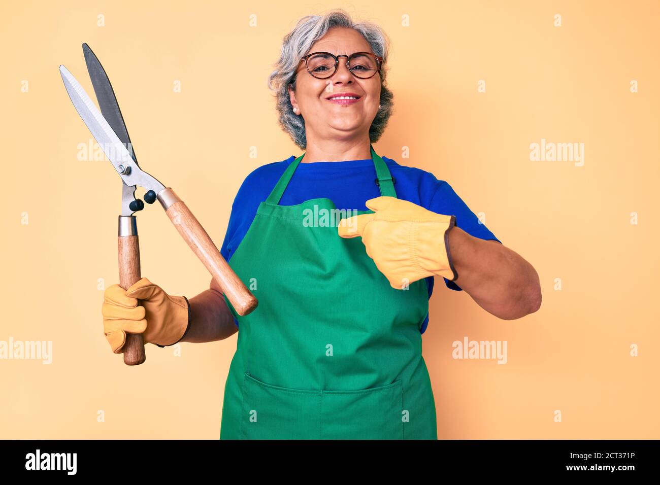 Senior hispanic woman wearing gardener apron and gloves holding shears ...