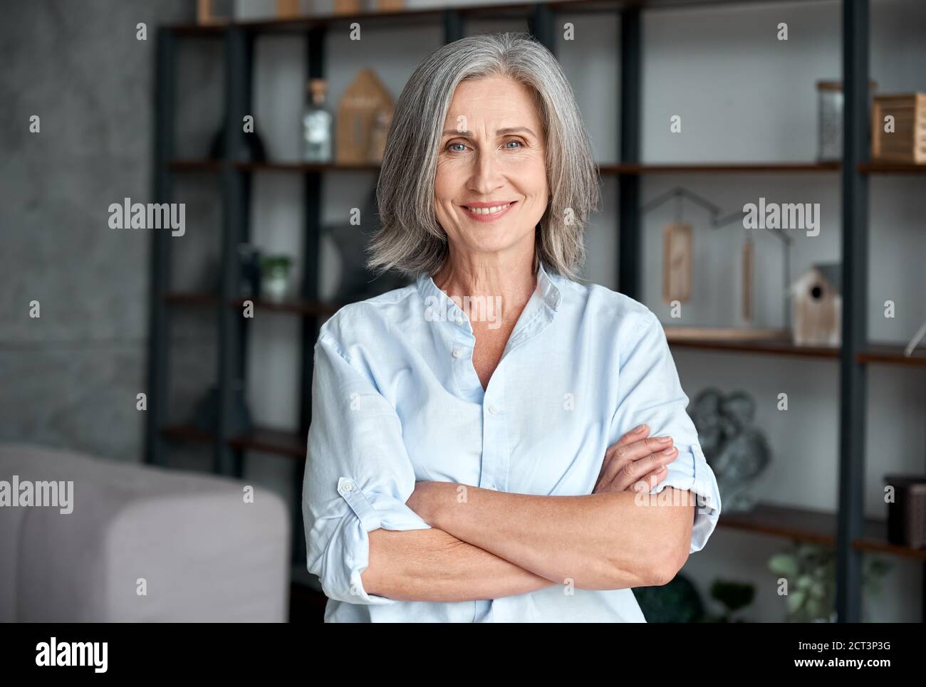 Smiling confident middle aged woman standing arms crossed in office, portrait. Stock Photo