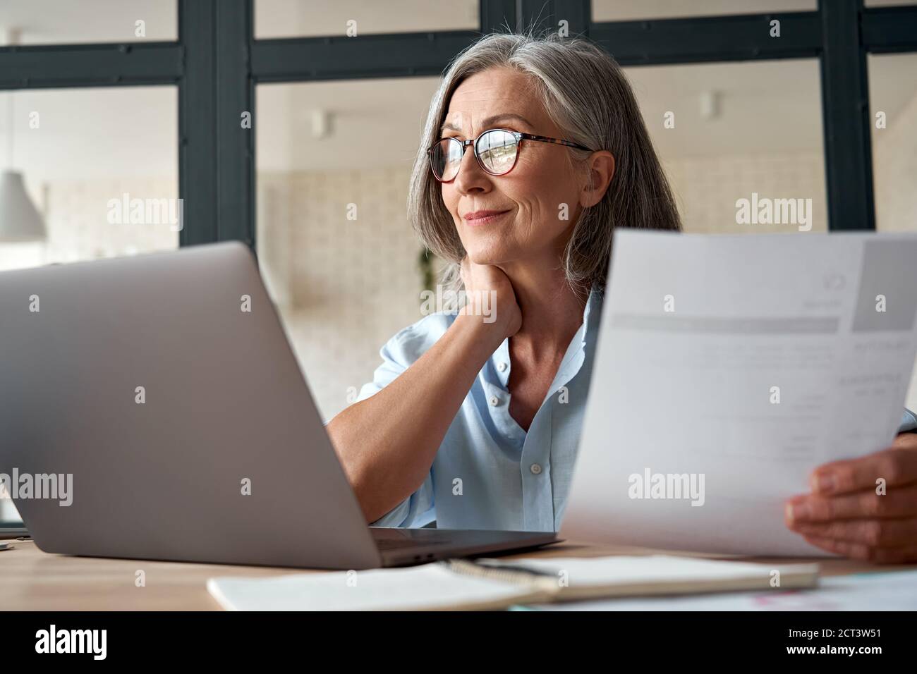 Smiling mature middle aged business woman holding cv searching job online. Stock Photo