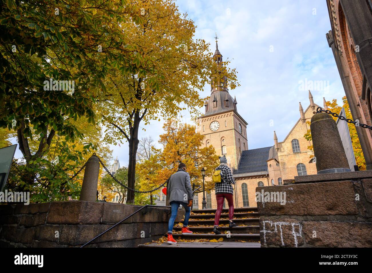 Two people are walking up the stairs to the Oslo Cathedral, located in the center of Oslo, Norway. In autumn, the leaves turn yellow and orange. Stock Photo