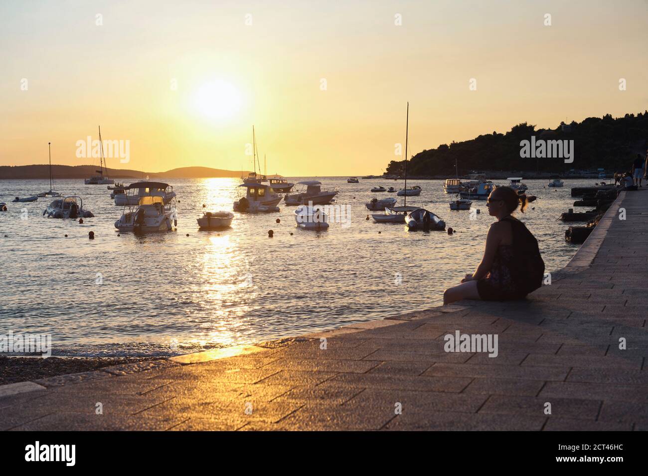 Photo of a tourist sitting watching the sunset in Hvar Town harbor ...