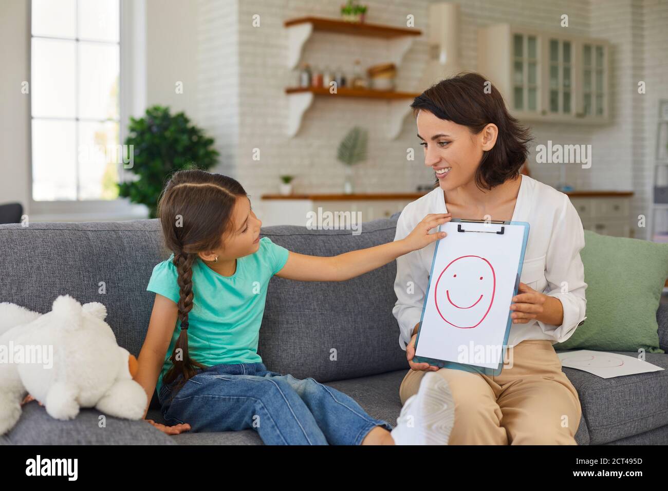 Private therapist talking to curious little girl during therapy session at home Stock Photo