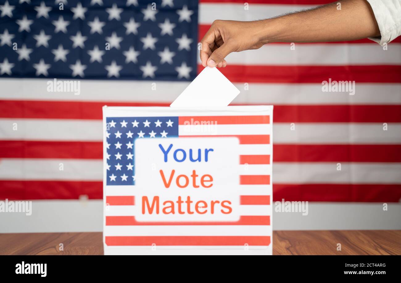Close up of Hands placing vote inside the Ballot box with your vote matters printed with US flag as background - Concept of voter rights and US Stock Photo