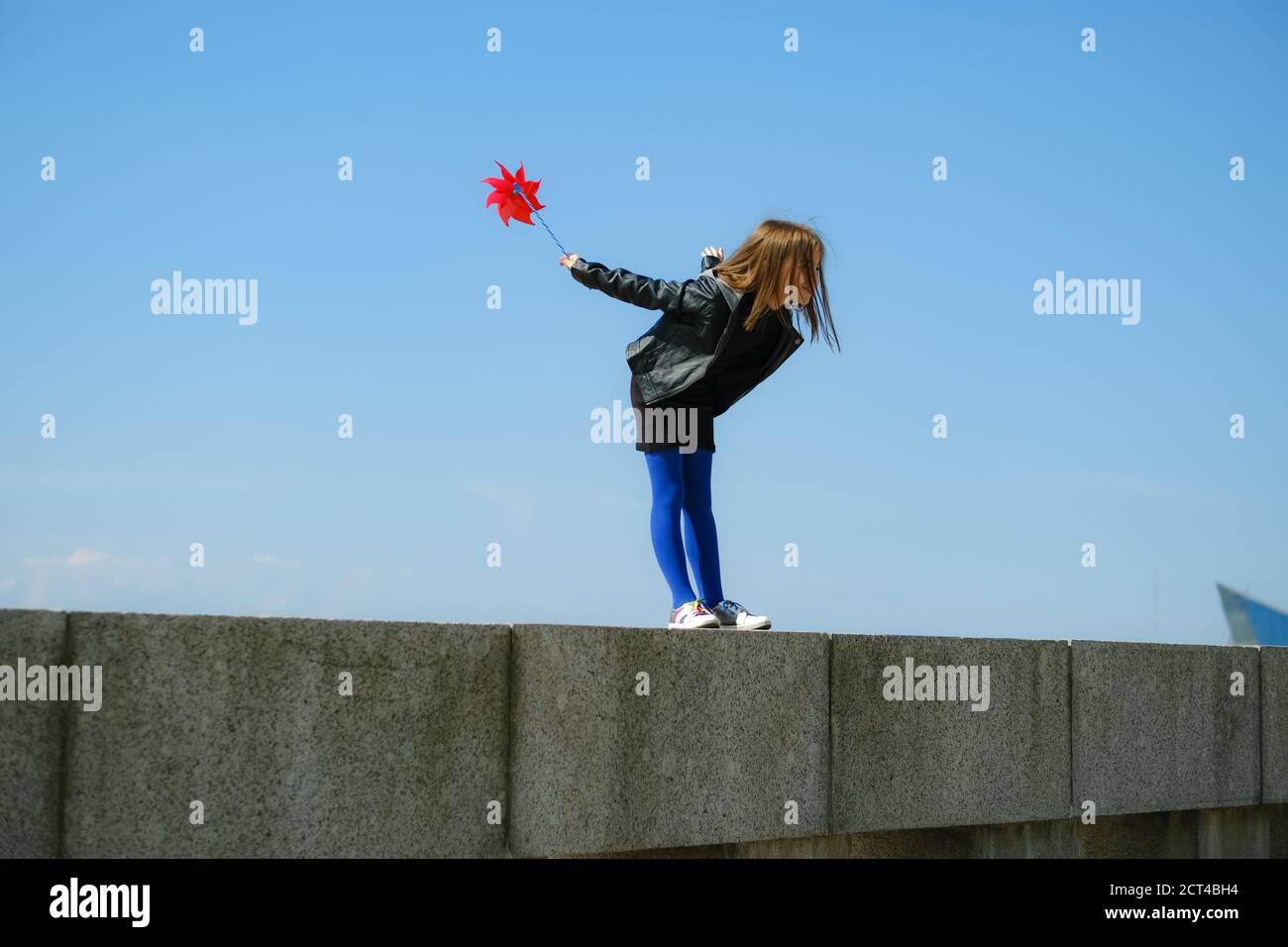 Happy girl with red wind spinner walking on the embankment on blue sky urban background. Freedom concept Stock Photo