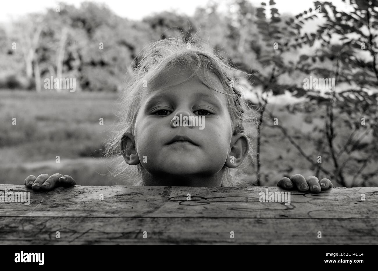 Close up black and white portrait of cute handsome Caucasian baby. Children's sincere emotions. Childhood moments. Girl near a wooden table at nature Stock Photo