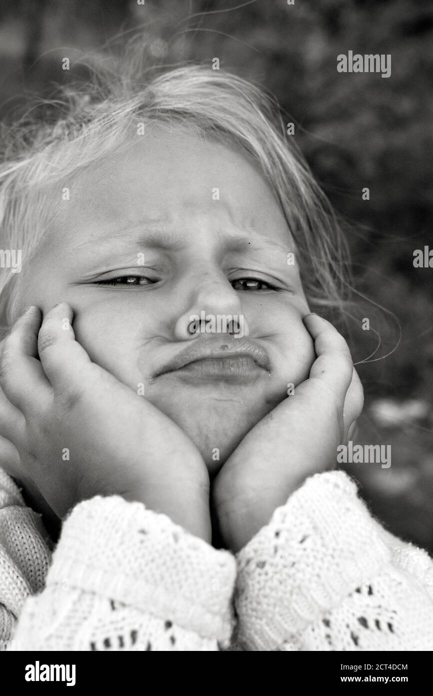 Close up black and white portrait of cute resentful and sad Caucasian child. Children's sincere emotions. Childhood moments. Child in nature. Stock Photo