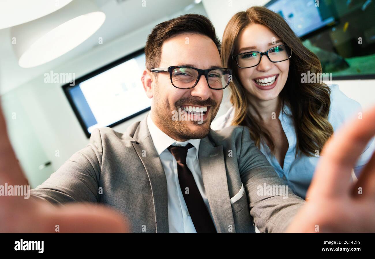 Smiling business couple using smart phone while taking selfie in office. Stock Photo