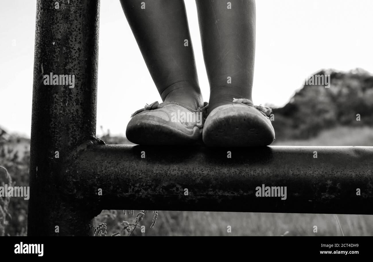 Close up black and white photo of a cute caucasian child. Childhood moments. The girl climbs and plays the iron pipe outdoors in the village. Baby Stock Photo