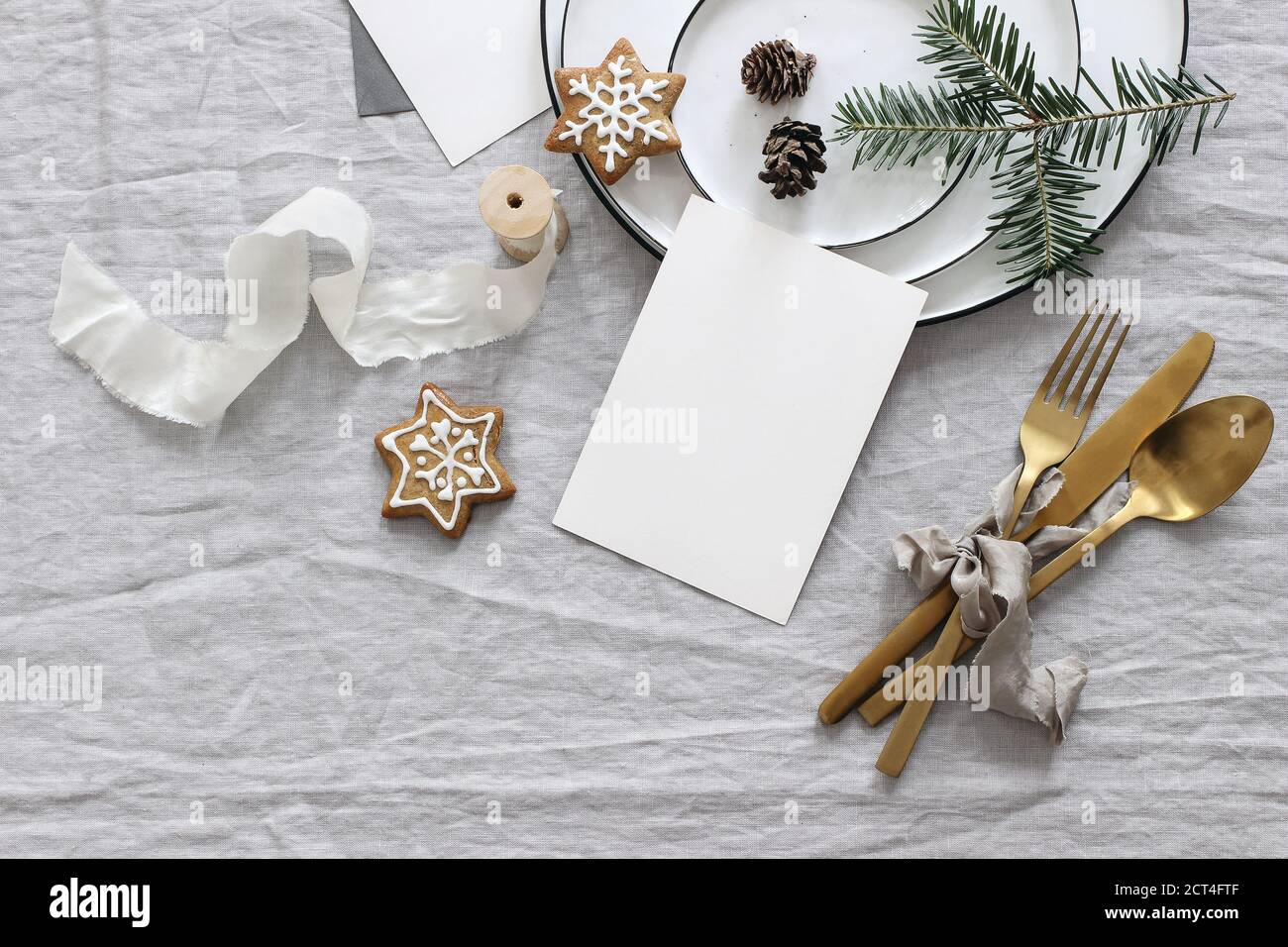 Plates, pine cones on table cloth. Winter festive greeting cards mockup scene. Golden cutlery,gingerbread cookies and fir tree branches. Christmas tab Stock Photo