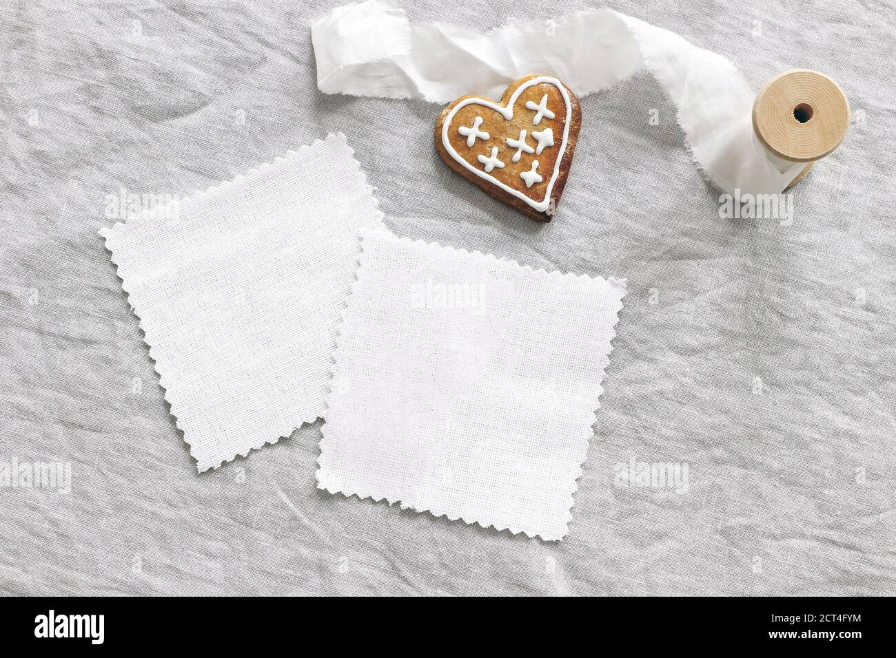 Christmas textile mockup scene. White cotton fabrics swatches on linen table cloth background. Gingerbread heart cookie, decorative sugar frosting and Stock Photo