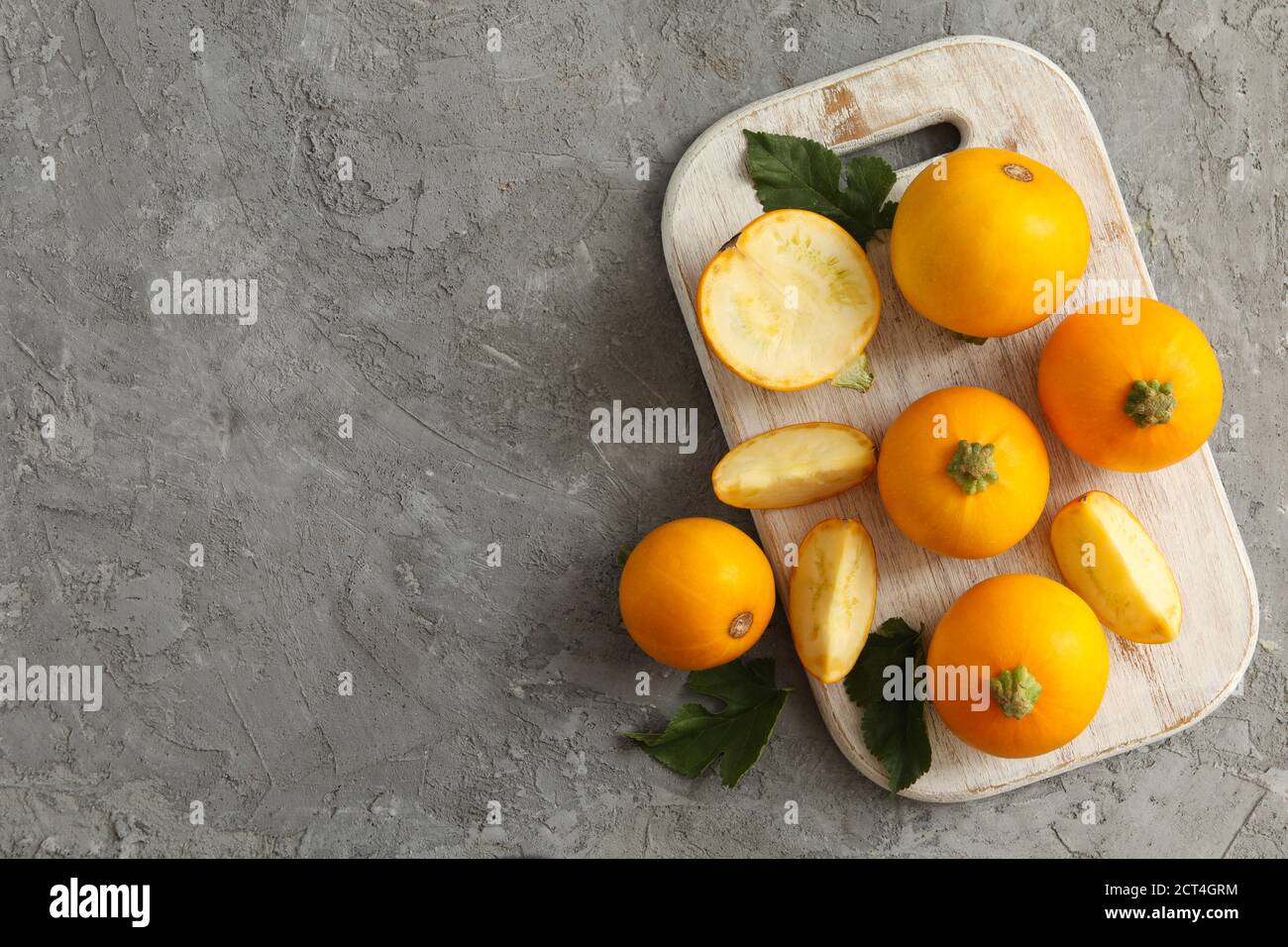 Board with round zucchini and leaves on gray background Stock Photo