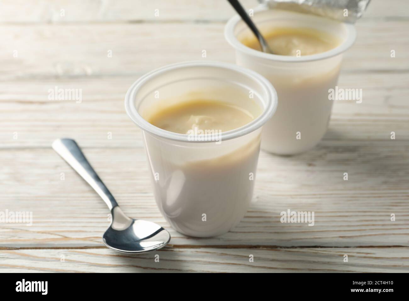 Plastic cups of yogurt and spoons on white wooden background Stock Photo Alamy