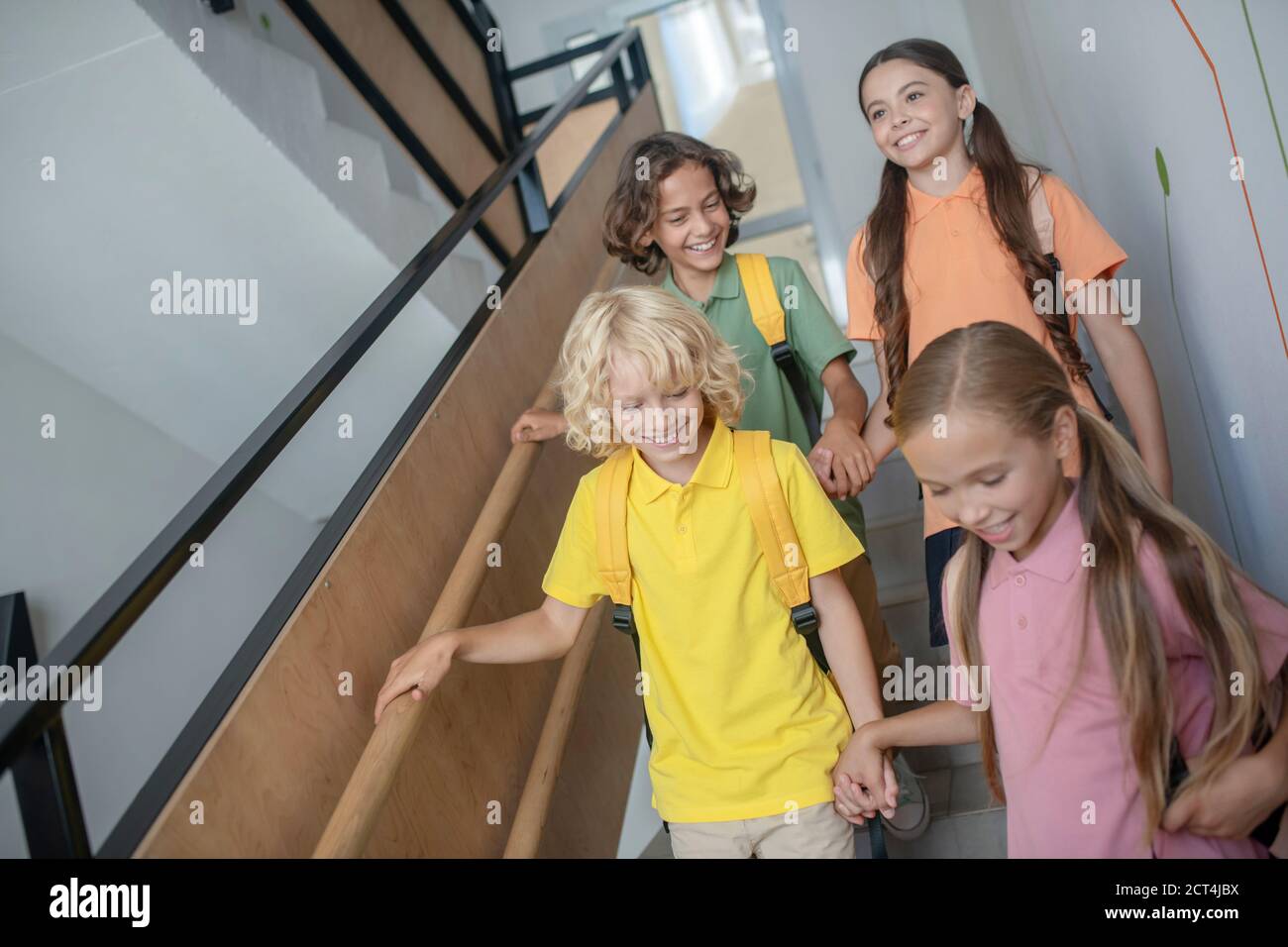 School friends going downstairs, holding hands and looking happy Stock Photo