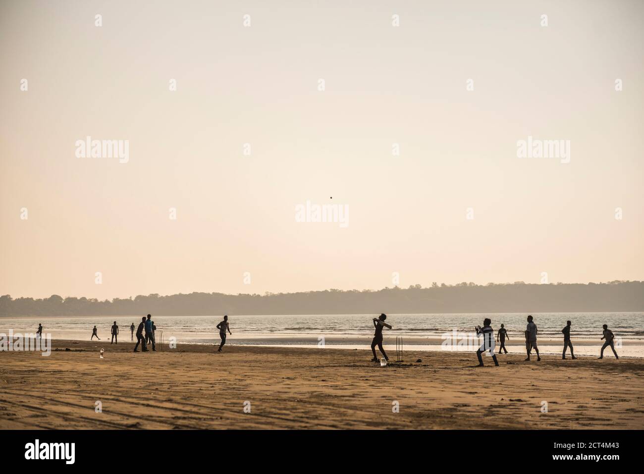 Street cricket in India, with a group playing as a batsman hits the ball on the beach at sunset under orange sky Stock Photo