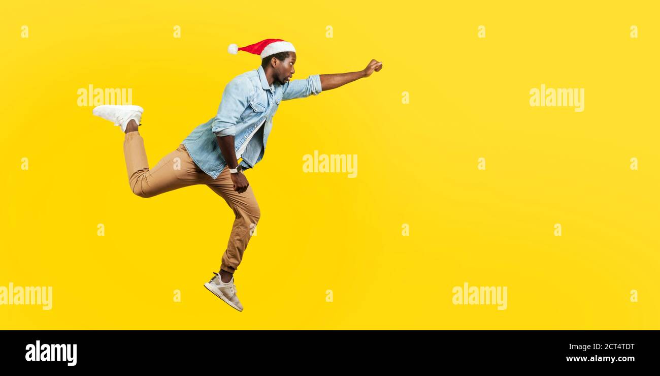 Full length portrait of handsome man in denim casual shirt and new year santa hat jumping in air or flying high with one stretched arm, feeling to be Stock Photo