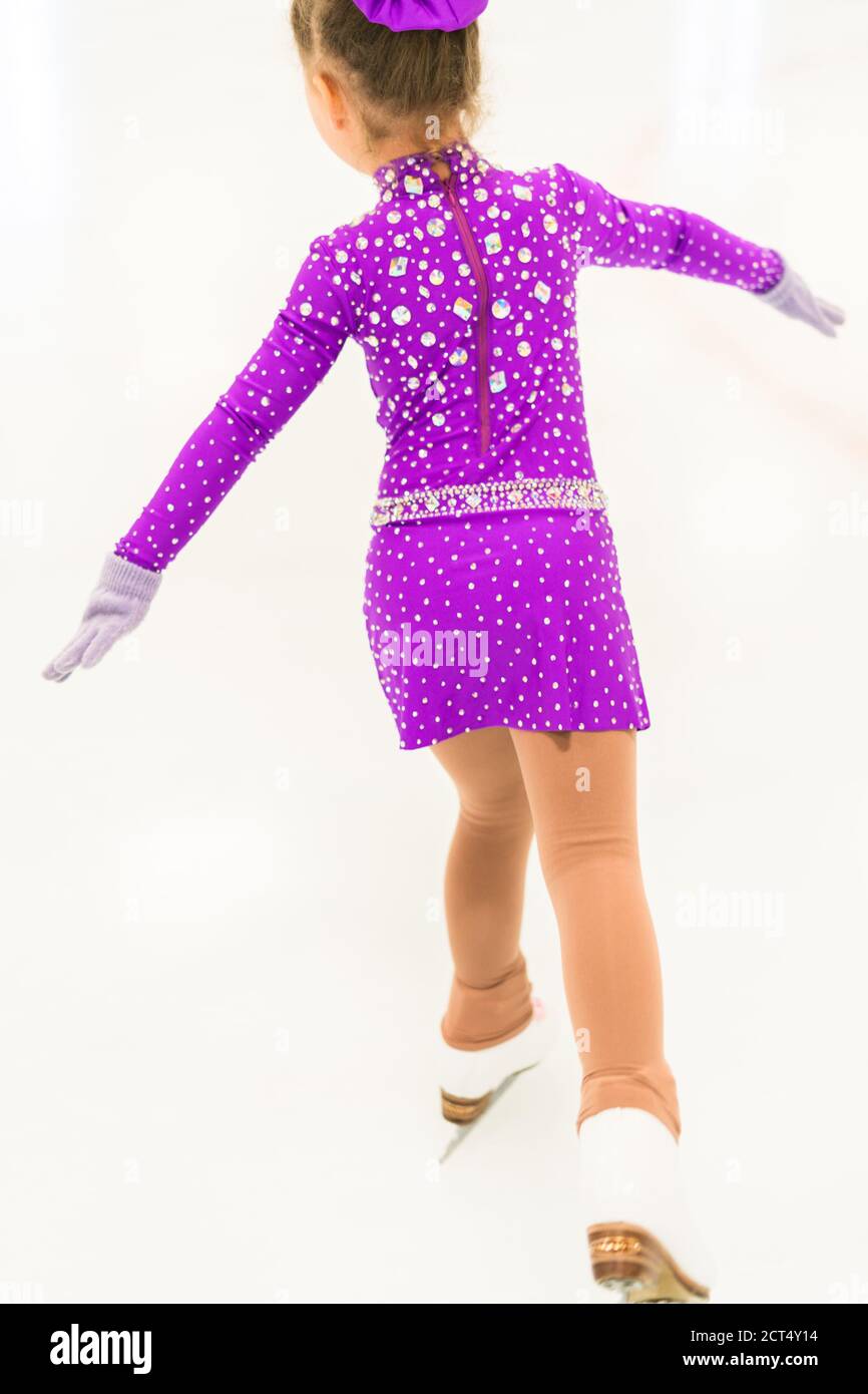 Little girl practicing figure skating in a purple dress with crystals