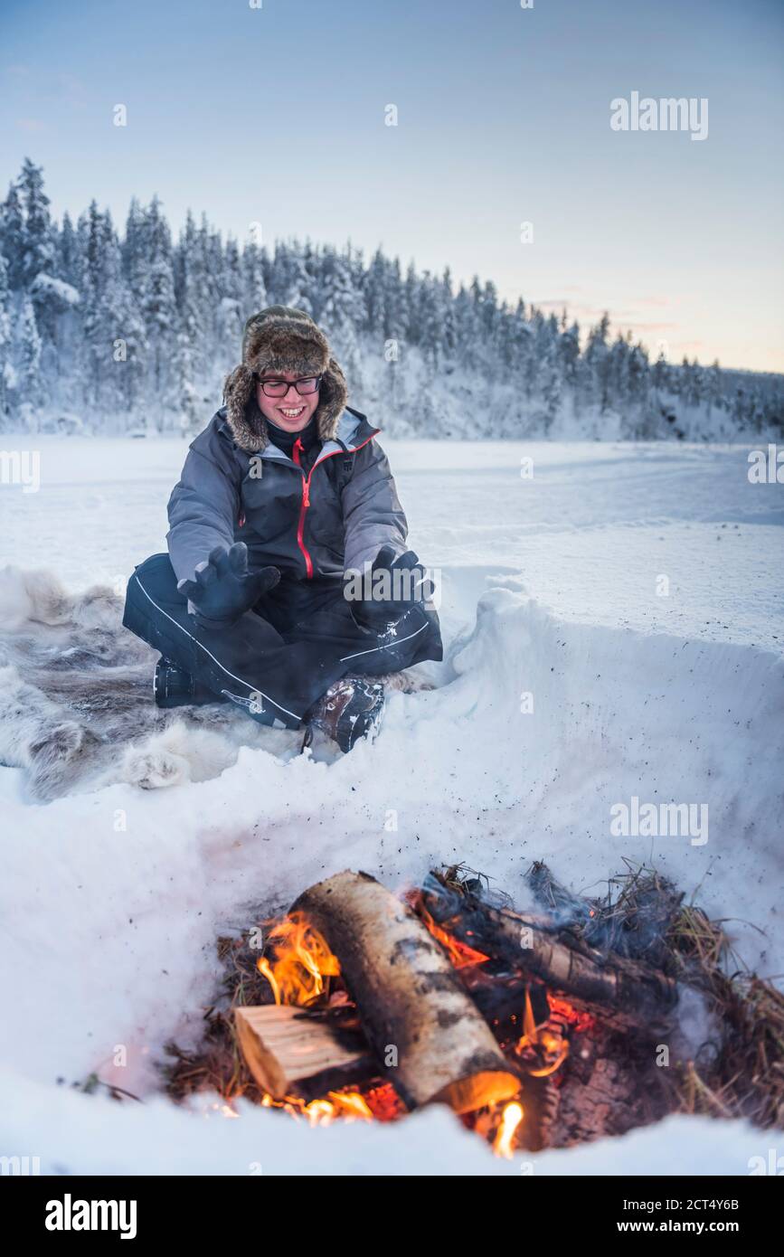 Person sat at a camp fire warming himself on a freezing cold day in winter in the Arctic Circle in Lapland, Finland Stock Photo