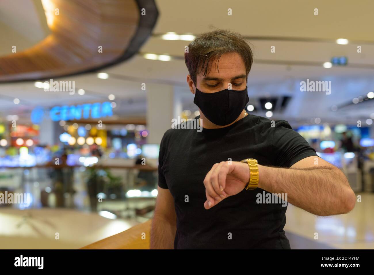 Portrait of Persian man with mask checking the time at the mall indoors Stock Photo