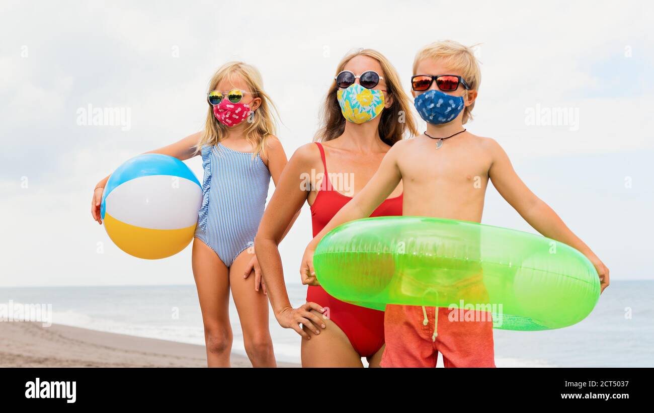 Funny children in sunglasses, inflatable toys on tropical sea beach. New rules to wear cloth face covering mask at public places due coronavirus COVID Stock Photo