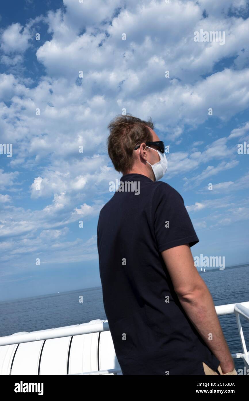 a middle aged french male passenger wearing a facial mask against Covid stands looking out to sea on a ferry in Brittany during summer holidays France Stock Photo