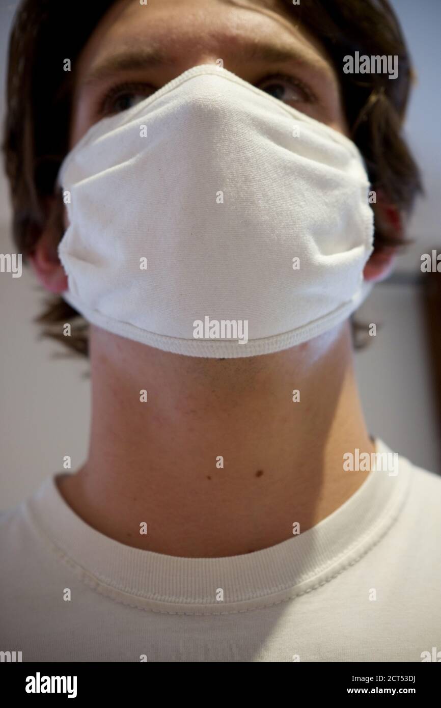 a close up of an eighteen year old man's face wearing a white cotton reusable anti viral mask Stock Photo