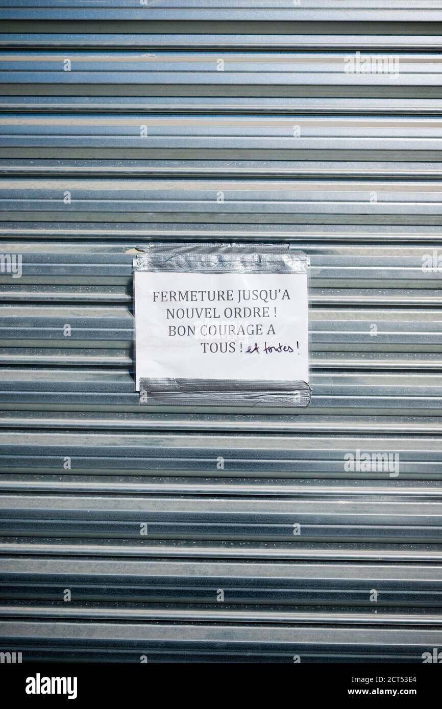 a printed sign in french with handwritten correction stuck on closed metal shutter of shop saying closed until further notice, all the best everyone! Stock Photo